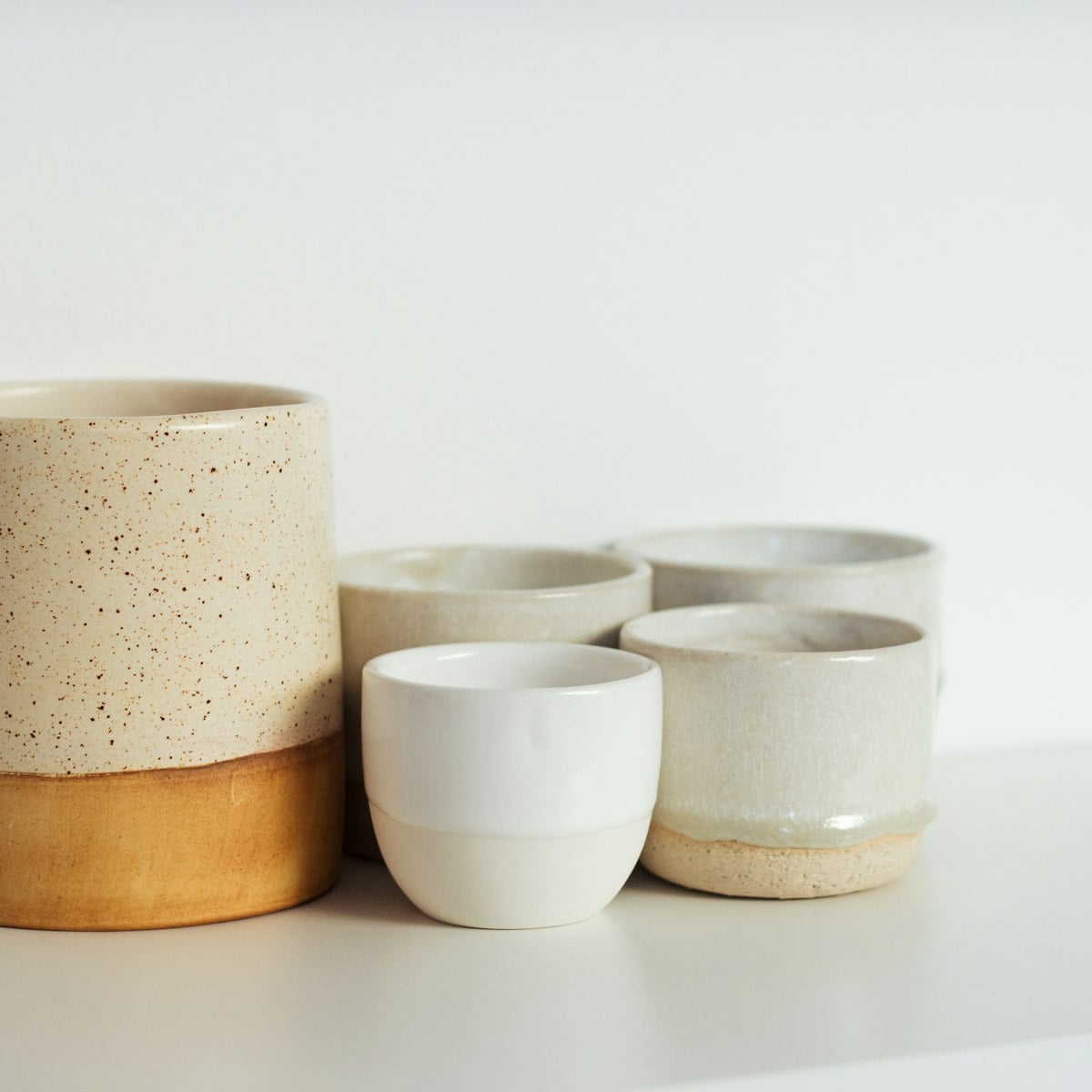 Trio de vasos de cerâmica artesanal em tons neutros sobre superfície clara